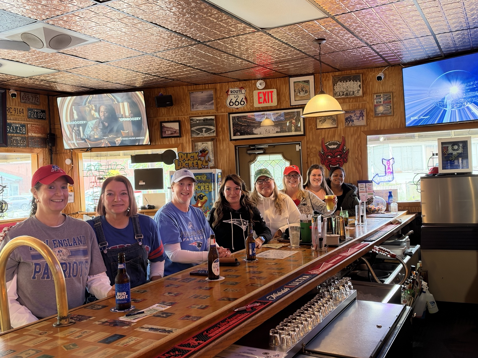 Friends at The Sixes Pub bar beneath sports screens and a copper ceiling